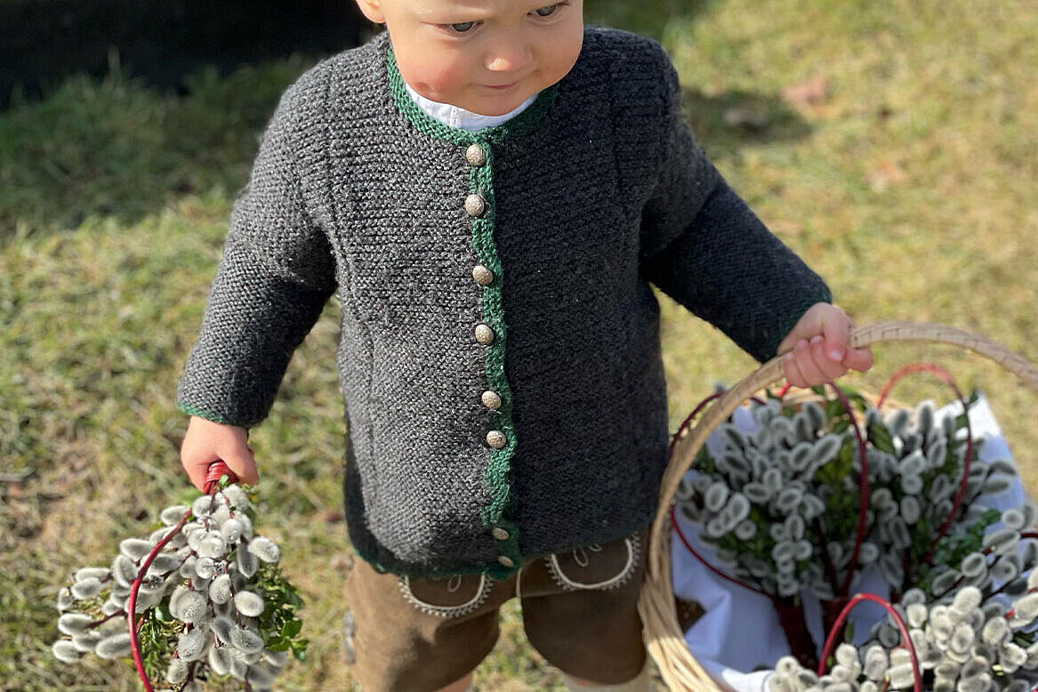 A child wearing traditional bavarian clothing holding catkins in its hands