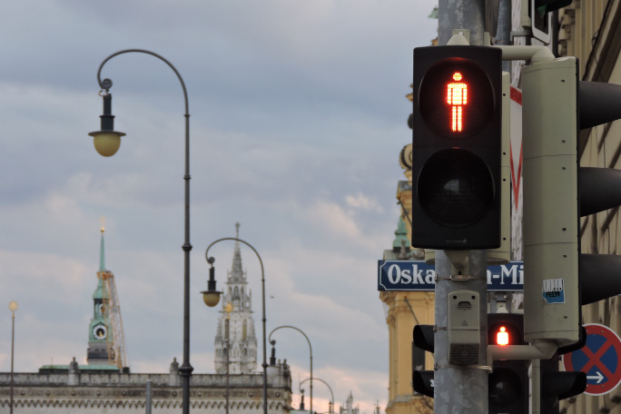 Red traffic light with skyline of Munich in the background.
