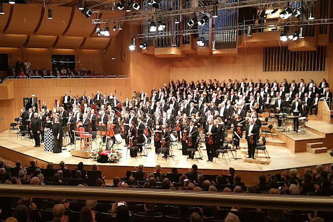 An orchestra enjoying applause from the public, seen from a seat in a concert hall.