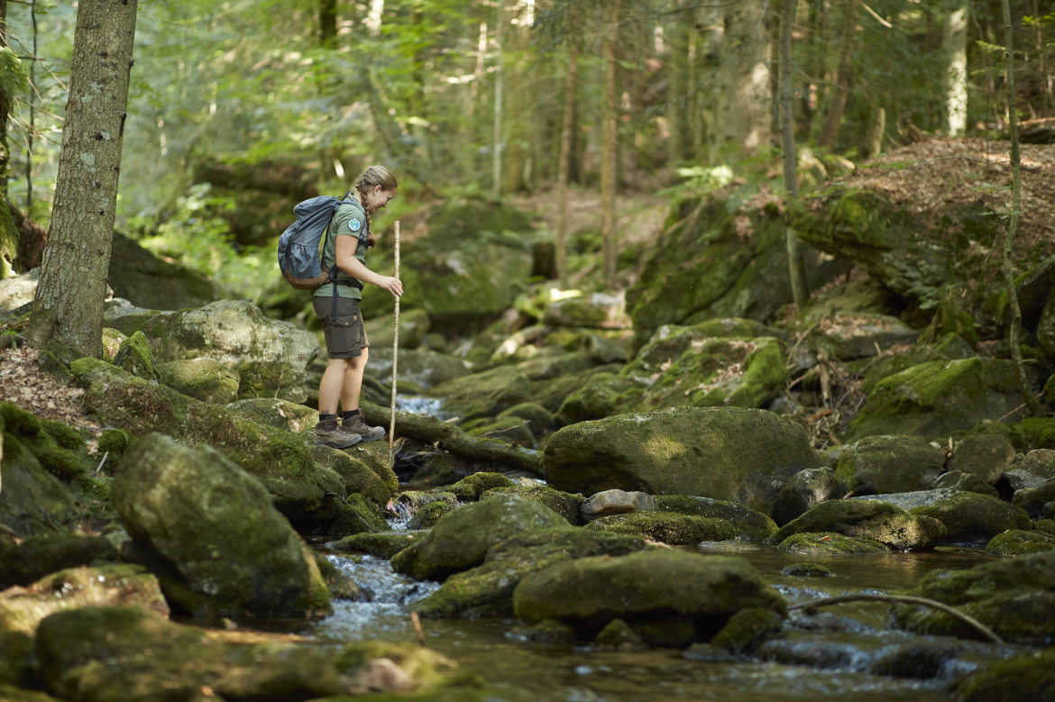 Female hiker crossing a stream in the Bavarian Forest.
