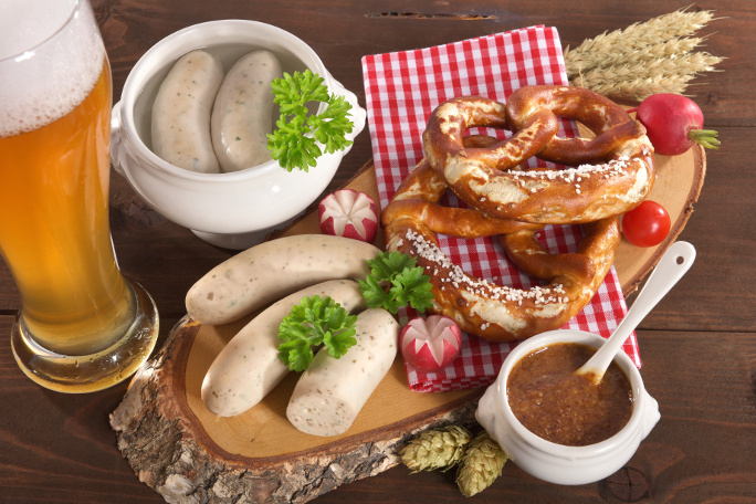 White sausages served in a bowl with sweet mustard, pretzels and a wheet beer.