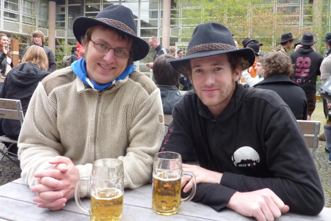 Two wood technology students with traditional hat in sitting together and drinking a beer