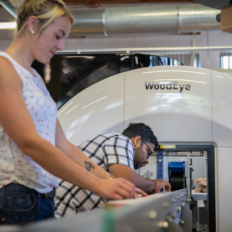 Two students working on wood technology, putting wood inside a machine