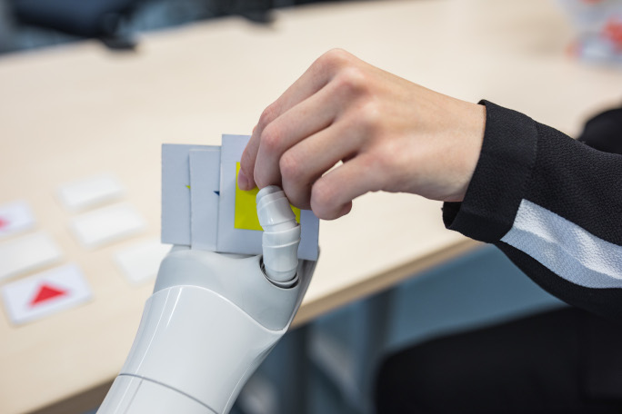 A human hand takes a card from a robot's hand.