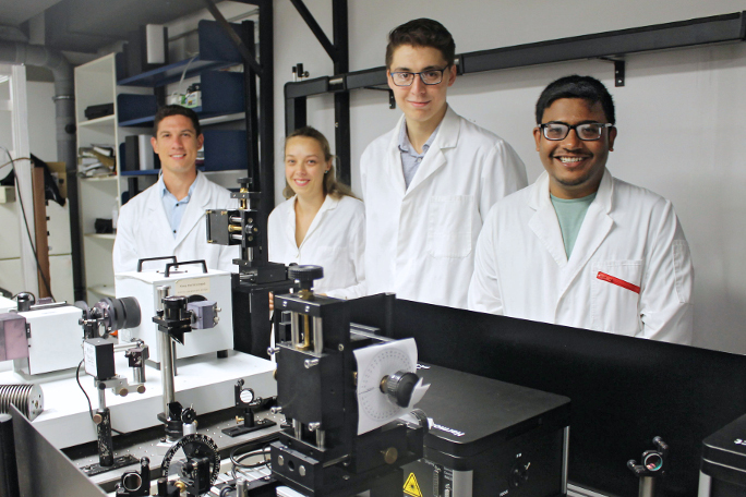 Four young researchers standing behind a machine