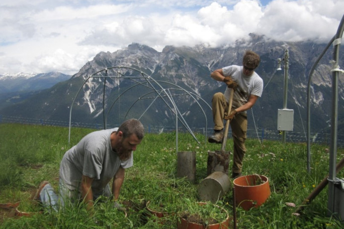 Two students working outdoors, with scenic panorama of the Alps in the background.