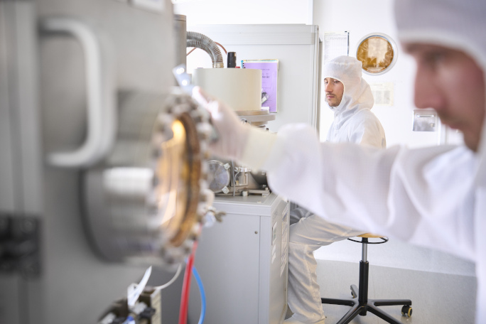 Two researchers, dressed in white protective suits, in a cleanroom