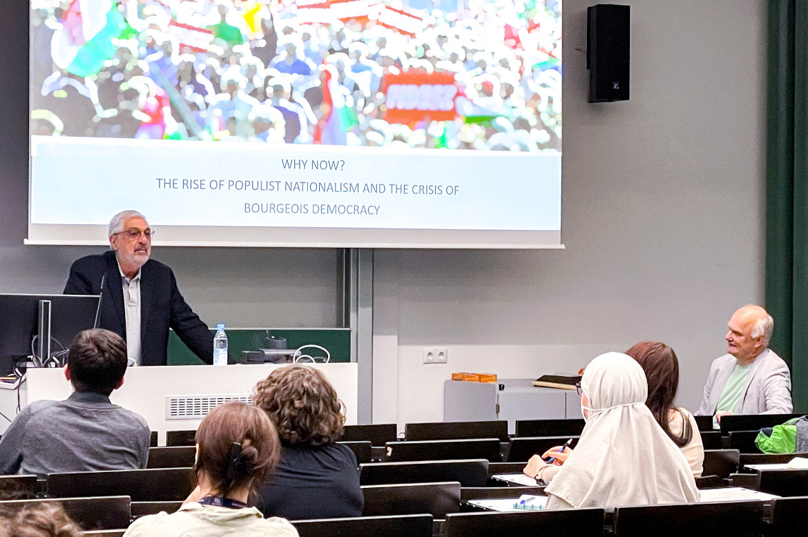 A Researchers giving a lecture. The title is shown in his presentation: "Why now? The rise of populist nationalism and the crisis of bourgeois democracy."
