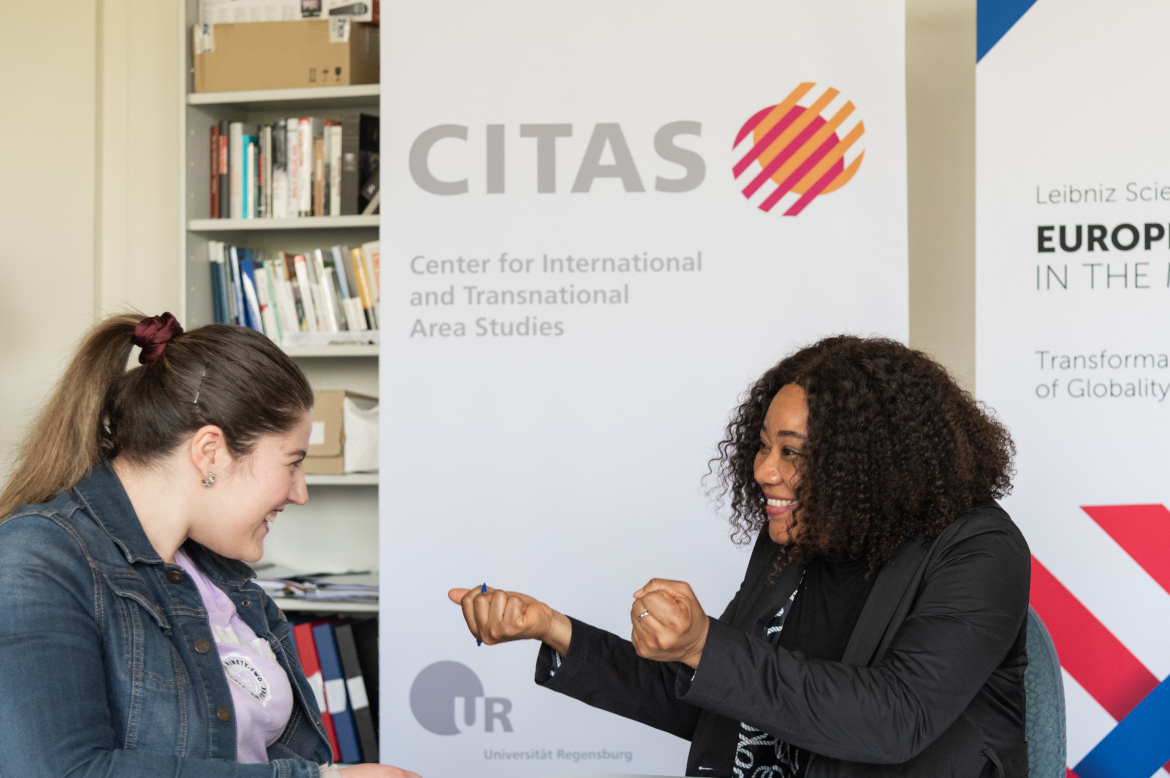 Two young researchers are discussing in front of a rollup: "CITAS - Center for International and Transnational Area Studies".