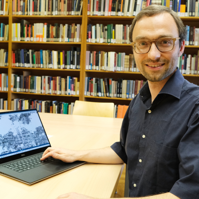 Researcher in ancient philology with his laptop displaying a fragment of a papyrus scroll.