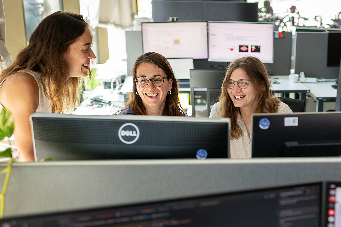 Three young female researchers are discussing while looking at a screen.
