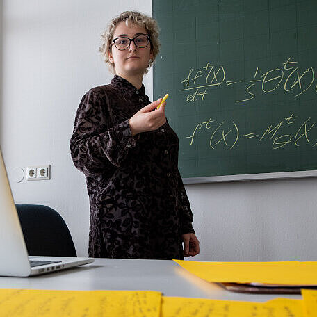 Mariia Seleznova writing formulas on a black board.