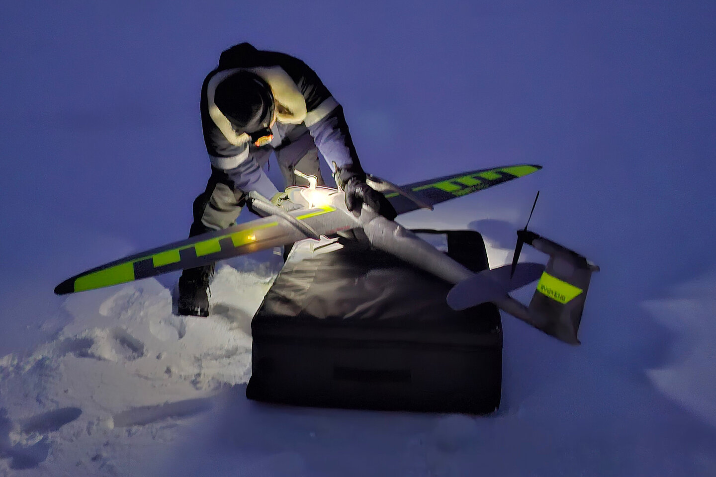 Against the backdrop of a dark, snowy landscape, a researcher prepares a drone to study the effects of climate change on ecosystems.