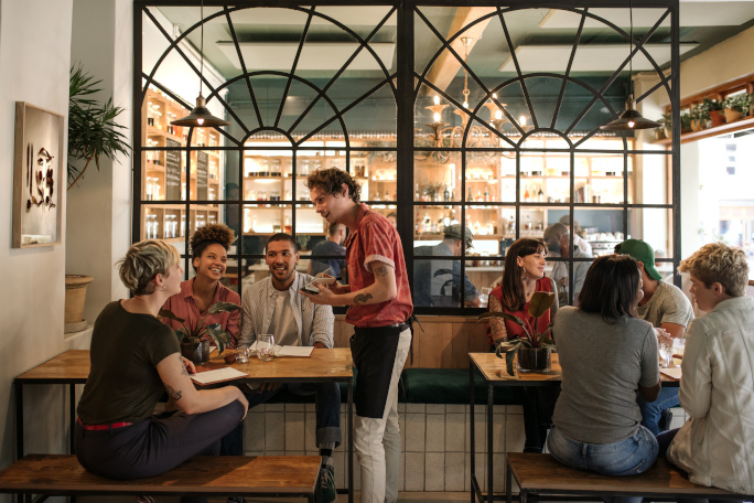 People chatting inside a coffee shop and a waiter taking the order of one group of people.