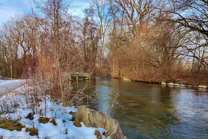 A river flowing through a park with trees and snow.