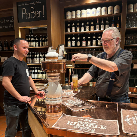 Filip Simonovski standing in front of a bar, behind it is a male brewer pouring beer from the tap