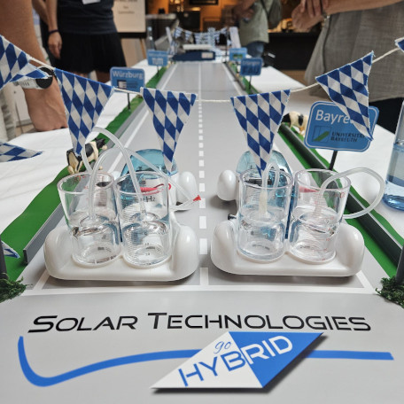 A demo from SolTech at their booth in the Lindau Nobel Laureate Meetings. From bottom to top: SolTech logo, two small futuristic looking cars on a track, Bavarian flags