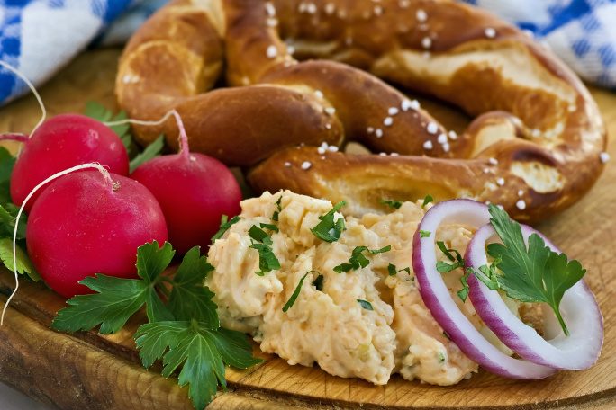 Obadzda served on a wooden board with onions and a pretzel.