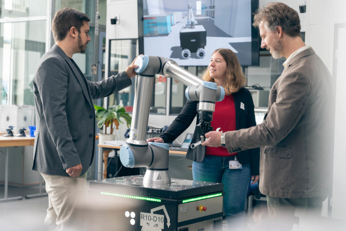 Three researchers testing a robot with wheels and a robot arm made for use of ai in production.