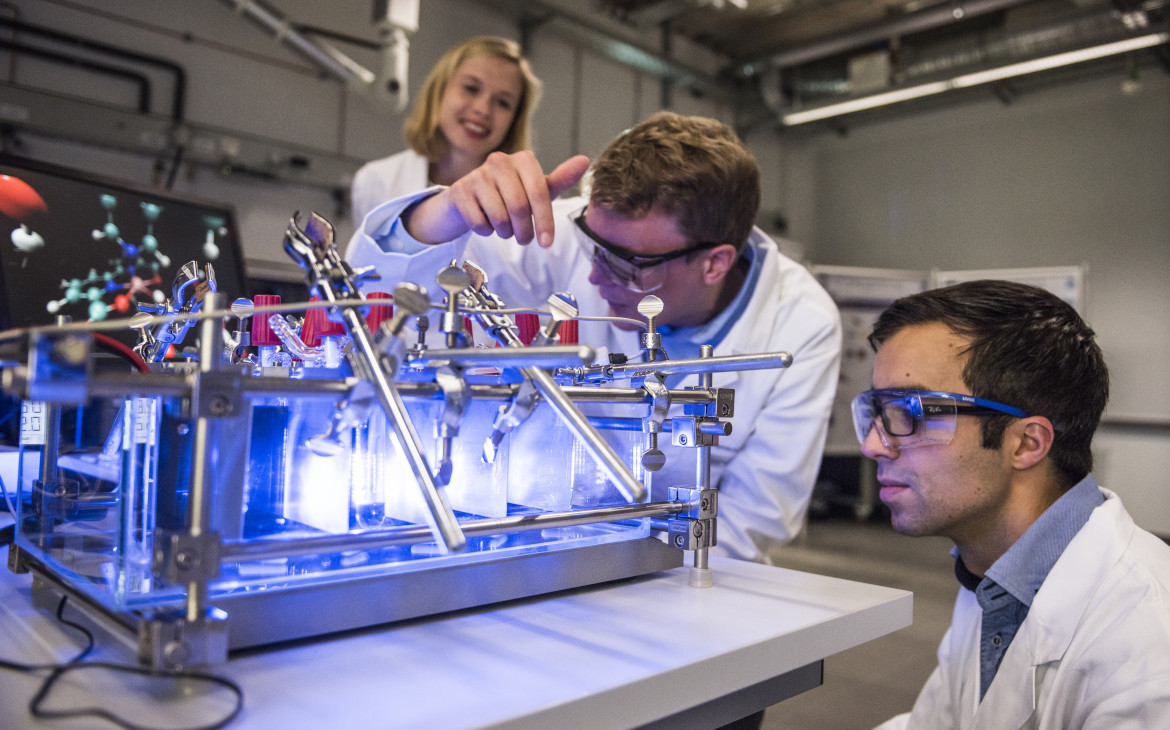 Three researchers looking at an experimental setup glowing in light blue.