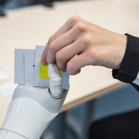 A robot's and a human's hand holding a card of a memory game.