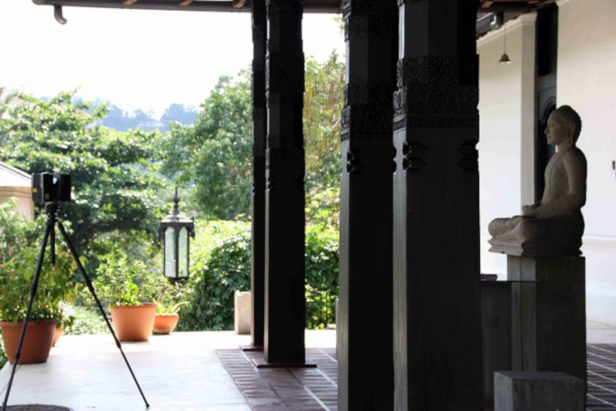 A camera in a temple in front of a sculpture with green woods in the background