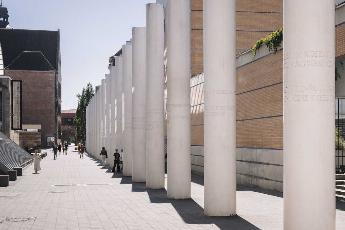 A line-up of white columns in a street. On each of them one article of the Universal Declaration of Human Rights in German and another language is engraved..