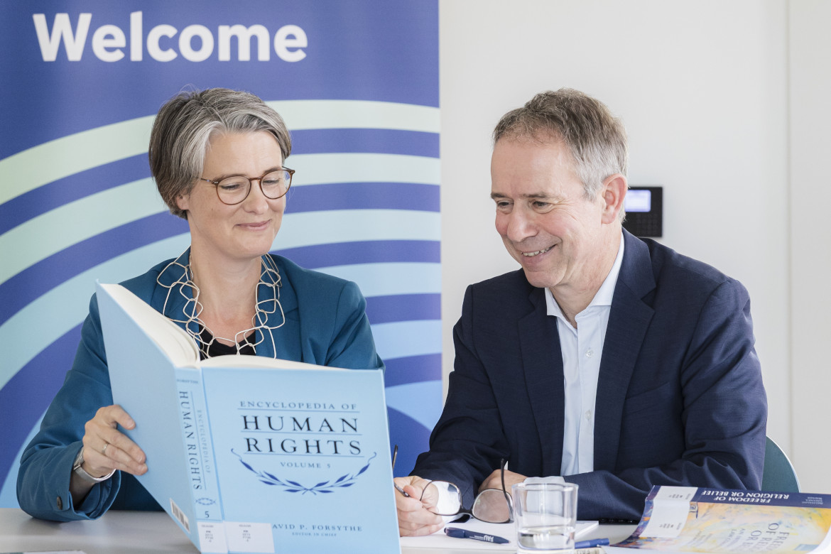 Two professors have a look into the Encyclopedia of Human Rights, Vol. 5 by David P. Forsythe. Behind them, a roll-up with the sign "Welcome". 