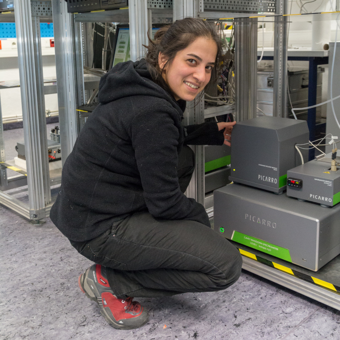 PhD researcher kneeing in front of machines.