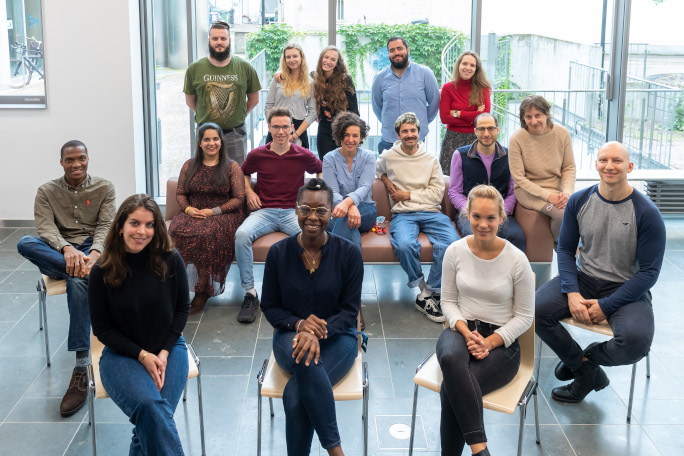 International group of 15 young researchers and their professor sitting on chairs for the foto.