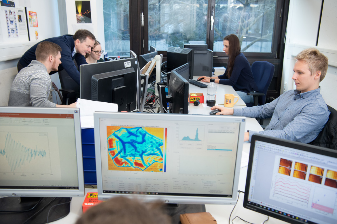 Computerscreens in the front, Prof. Huber working with researchers in the back