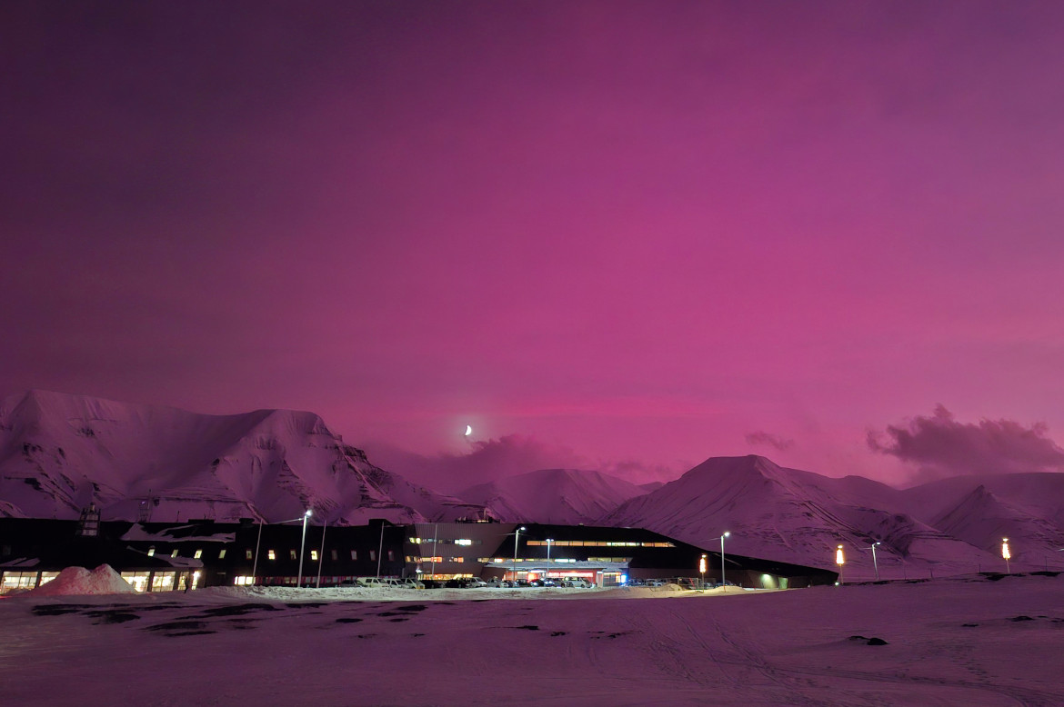 A research station surrounded by snow-capped mountains under a violet sky with a half moon.