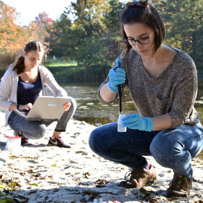 Two international, female scientists taking and documenting laboratory samples at a lake.