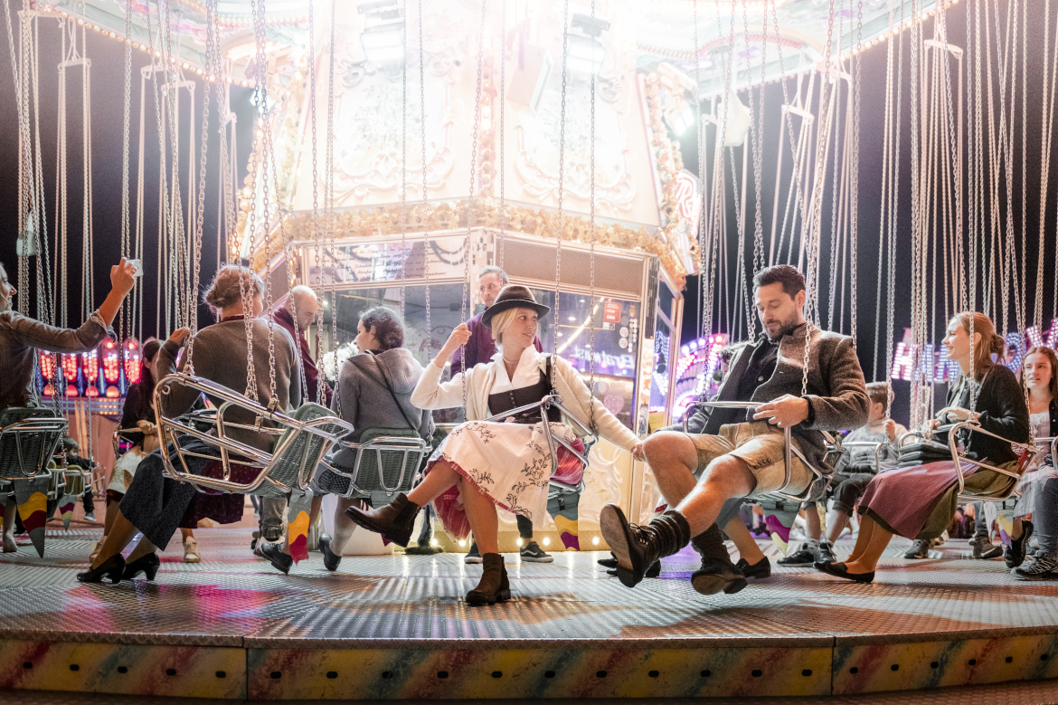 Group of young people wearing traditional garb on a swing ride at a beer festival.