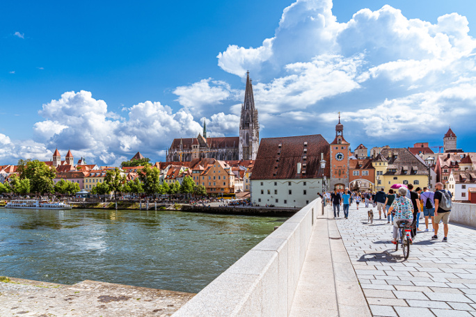 People crossing the Stone Bridge in Regensburg on a summer day.