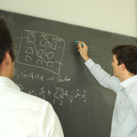 A reseacher and Professor Mauerer writing a mathematical formula on a blackboard. Their aim is to develop quantum applications for industry.