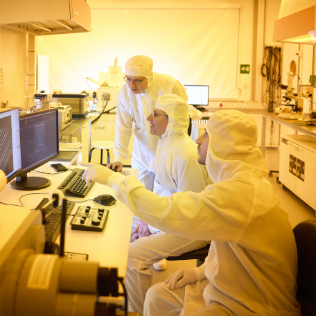 Dmitri Efetov discusses with two colleagues, dressed in white protective suits researching on graphene