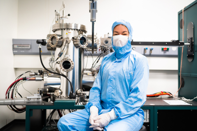 Prof. Eva Weig wearing a cleanroom overall sitting on a chair in front of a machine