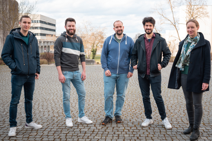 Five researchers of the new Faculty of Informatics and Data Sciences stand on the campus of the University of Regensburg and smile at the camera.